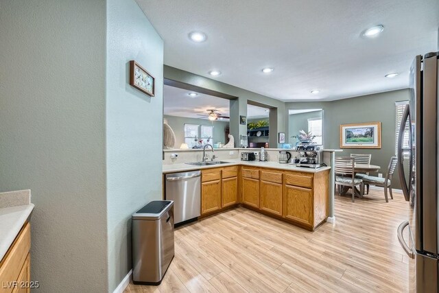 kitchen with kitchen peninsula, appliances with stainless steel finishes, a healthy amount of sunlight, light wood-type flooring, and sink