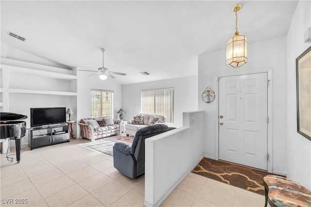 living room with lofted ceiling, built in shelves, light tile patterned flooring, and ceiling fan with notable chandelier