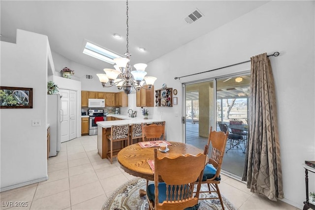 dining area featuring sink, vaulted ceiling with skylight, light tile patterned flooring, and an inviting chandelier