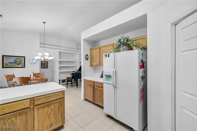 kitchen with white fridge with ice dispenser, tile counters, hanging light fixtures, built in features, and a notable chandelier