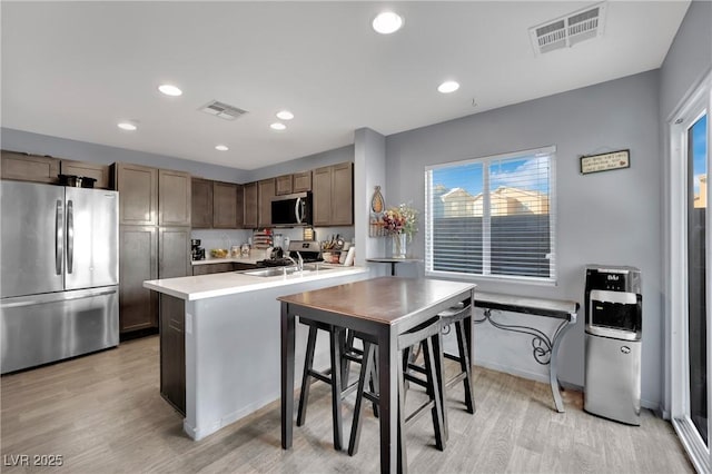 kitchen with sink, appliances with stainless steel finishes, light hardwood / wood-style flooring, and an island with sink