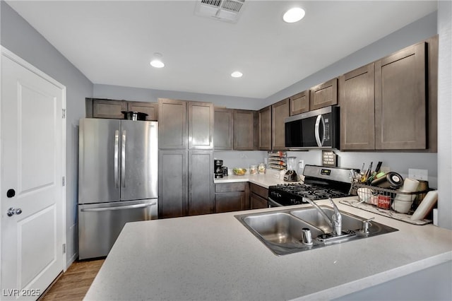 kitchen featuring appliances with stainless steel finishes, light hardwood / wood-style floors, sink, kitchen peninsula, and dark brown cabinets