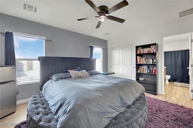 bedroom with ceiling fan, ensuite bathroom, multiple windows, and light hardwood / wood-style flooring