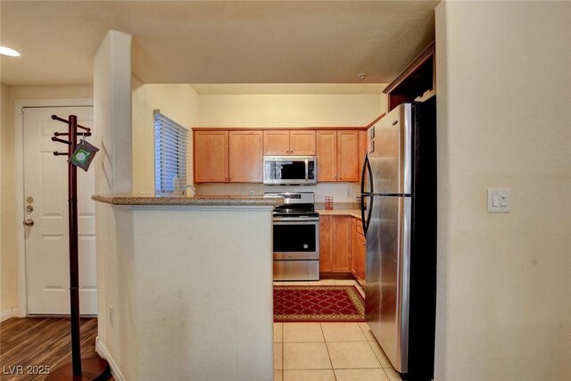 kitchen featuring light tile patterned floors, kitchen peninsula, and appliances with stainless steel finishes