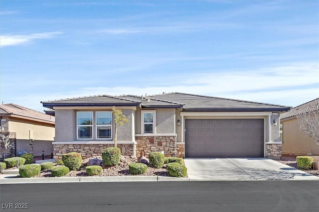 prairie-style home featuring an attached garage, stone siding, concrete driveway, and stucco siding