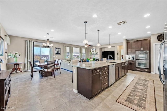 kitchen featuring ceiling fan with notable chandelier, a large island with sink, appliances with stainless steel finishes, sink, and hanging light fixtures