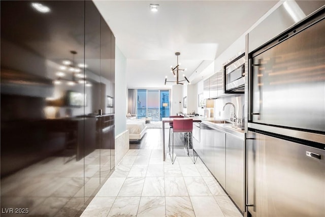 kitchen with a breakfast bar area, stainless steel appliances, hanging light fixtures, a chandelier, and sink