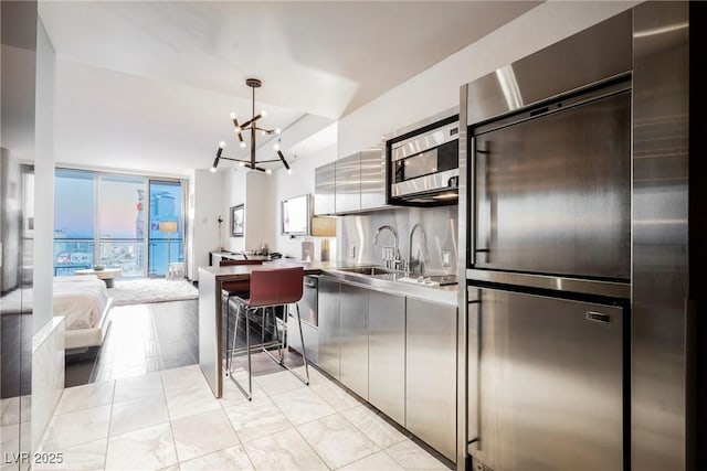 kitchen featuring an inviting chandelier, appliances with stainless steel finishes, a wall of windows, hanging light fixtures, and sink