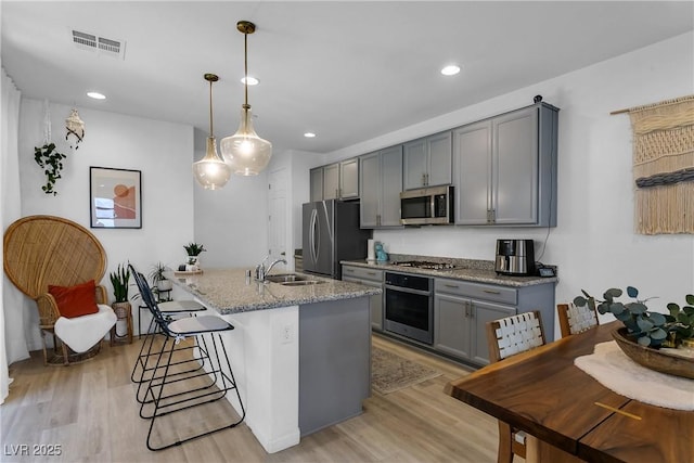 kitchen featuring light stone countertops, appliances with stainless steel finishes, hanging light fixtures, gray cabinets, and light wood-type flooring