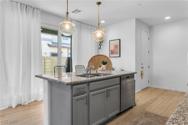 kitchen featuring pendant lighting, stainless steel dishwasher, sink, light wood-type flooring, and an island with sink