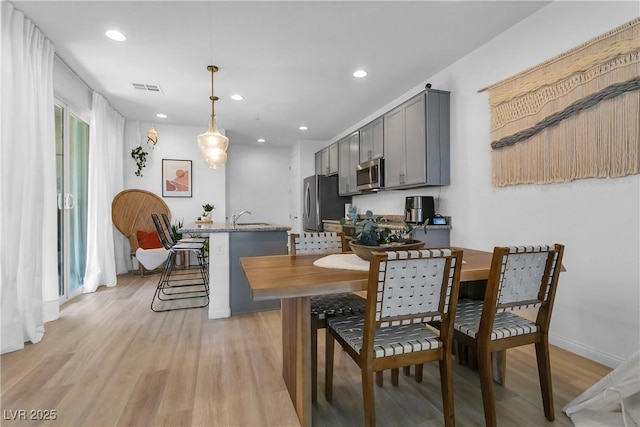 kitchen featuring hanging light fixtures, a kitchen breakfast bar, gray cabinetry, stainless steel appliances, and light stone counters