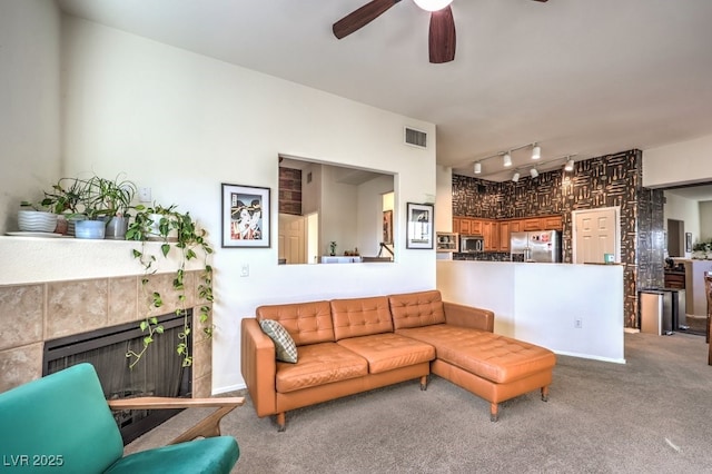 carpeted living room featuring ceiling fan, track lighting, and a tiled fireplace