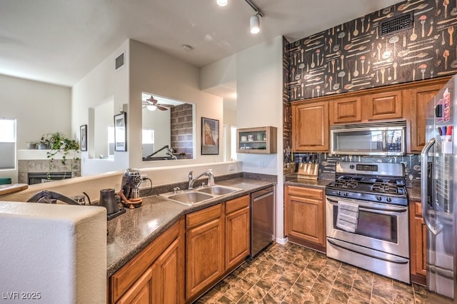 kitchen with ceiling fan, a tile fireplace, sink, track lighting, and stainless steel appliances