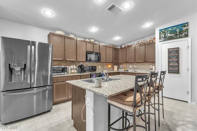 kitchen with an island with sink, light stone countertops, black appliances, a breakfast bar, and sink