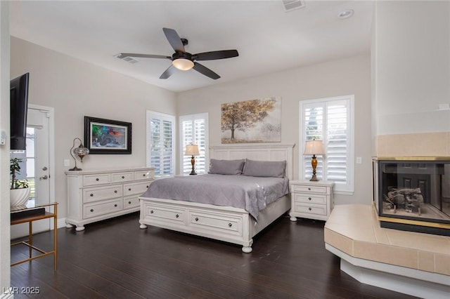 bedroom featuring multiple windows, ceiling fan, dark hardwood / wood-style floors, and a tile fireplace