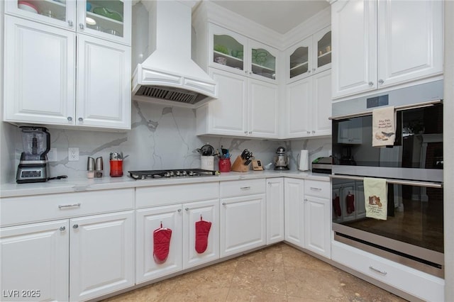 kitchen featuring white cabinetry, premium range hood, appliances with stainless steel finishes, and decorative backsplash