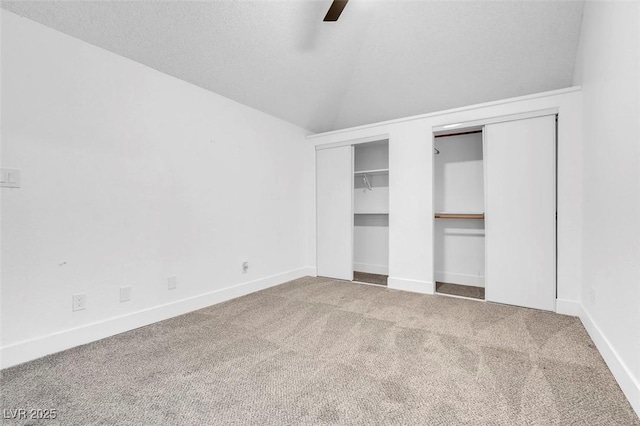 unfurnished bedroom featuring a textured ceiling, lofted ceiling, carpet floors, ceiling fan, and multiple closets