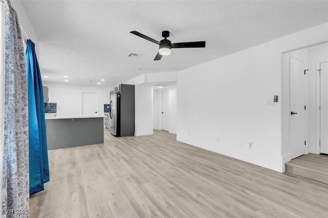 unfurnished living room with a textured ceiling, ceiling fan, and light hardwood / wood-style floors