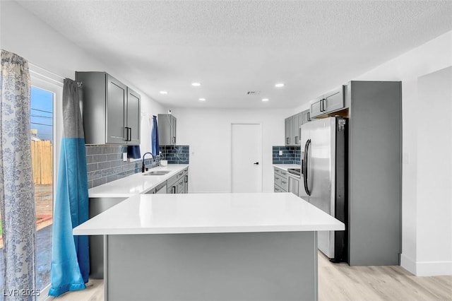 kitchen featuring a textured ceiling, stainless steel refrigerator with ice dispenser, tasteful backsplash, gray cabinets, and light hardwood / wood-style flooring