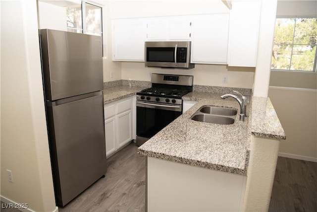 kitchen with light stone countertops, white cabinets, appliances with stainless steel finishes, sink, and kitchen peninsula