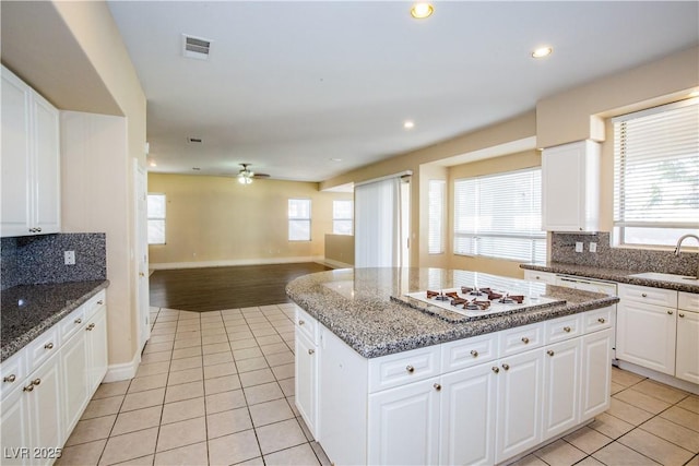 kitchen with white cabinets, a kitchen island, light tile patterned flooring, and sink