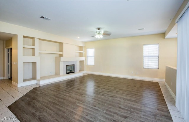 unfurnished living room with a premium fireplace, built in shelves, a wealth of natural light, and light tile patterned floors