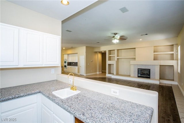 kitchen with white cabinetry, a tile fireplace, sink, built in shelves, and kitchen peninsula