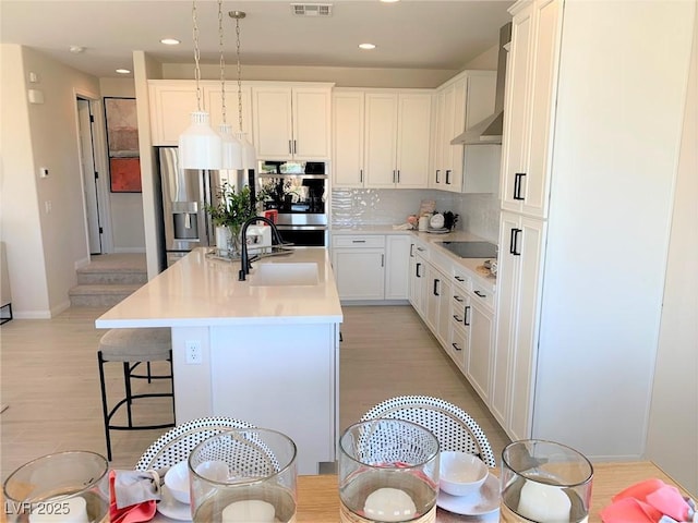 kitchen featuring sink, decorative light fixtures, appliances with stainless steel finishes, a kitchen island with sink, and white cabinets