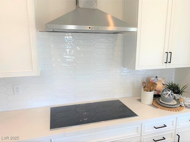 kitchen with black electric stovetop, white cabinets, backsplash, and wall chimney exhaust hood