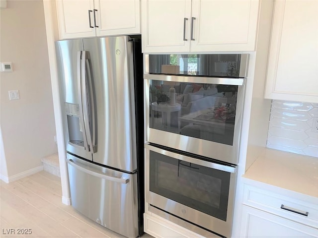 kitchen with tasteful backsplash, appliances with stainless steel finishes, white cabinets, and light hardwood / wood-style floors