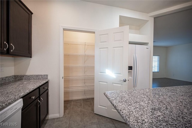 kitchen featuring stone countertops, white refrigerator with ice dispenser, dark brown cabinets, and dishwashing machine