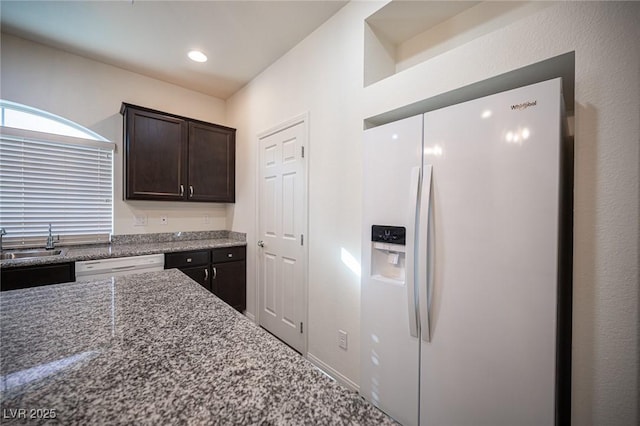 kitchen featuring white appliances, light stone counters, dark brown cabinets, a sink, and recessed lighting