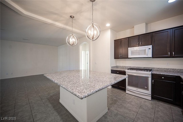 kitchen featuring arched walkways, a kitchen island, dark brown cabinetry, light stone countertops, and white appliances