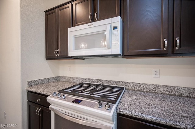 kitchen with gas stove, dark brown cabinetry, and white microwave