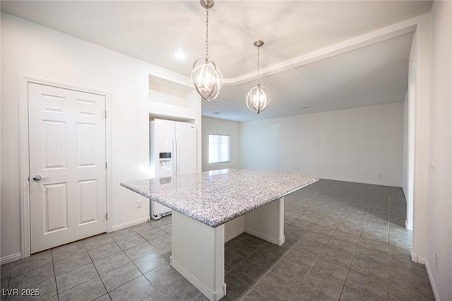 kitchen featuring a center island, white refrigerator with ice dispenser, hanging light fixtures, light stone countertops, and dark tile patterned flooring