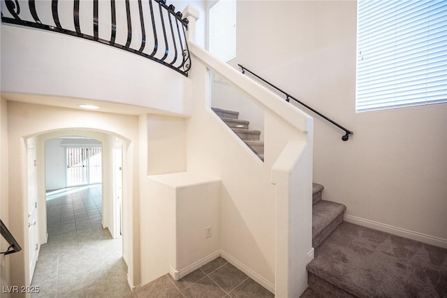 staircase featuring tile patterned floors, baseboards, and arched walkways