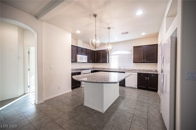 kitchen featuring dark brown cabinetry, white appliances, visible vents, arched walkways, and a kitchen island