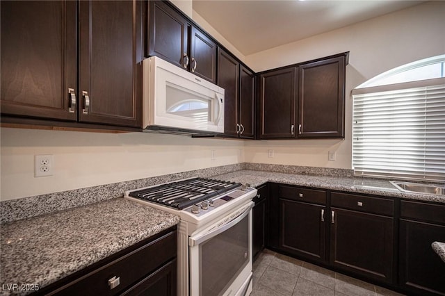 kitchen with white appliances, light tile patterned flooring, dark brown cabinetry, and a sink