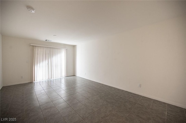 empty room with dark tile patterned floors, visible vents, and baseboards