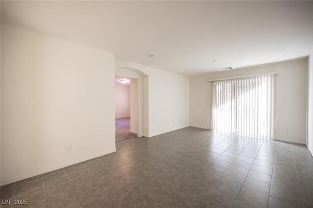 spare room featuring arched walkways, visible vents, baseboards, and dark tile patterned flooring