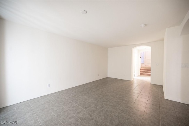 spare room with arched walkways, stairway, and tile patterned floors