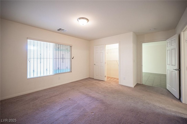 unfurnished bedroom with carpet floors, a walk in closet, visible vents, and baseboards