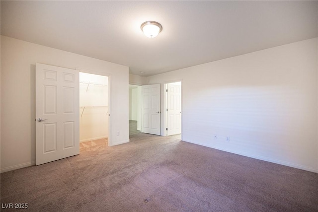 unfurnished bedroom with a closet, a spacious closet, baseboards, and carpet flooring