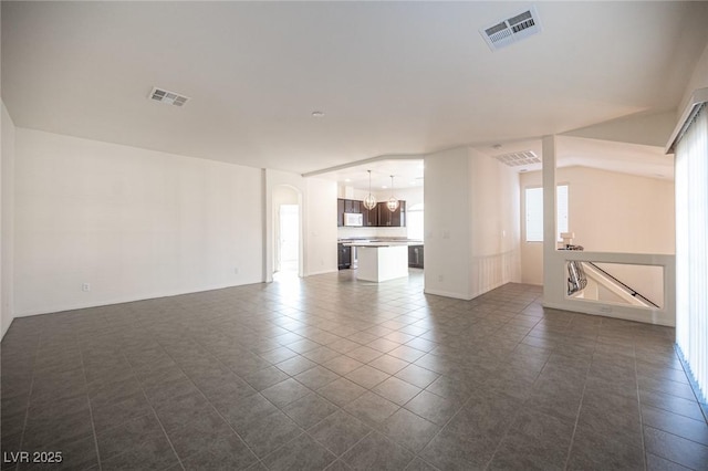 unfurnished living room with dark tile patterned flooring, visible vents, and arched walkways