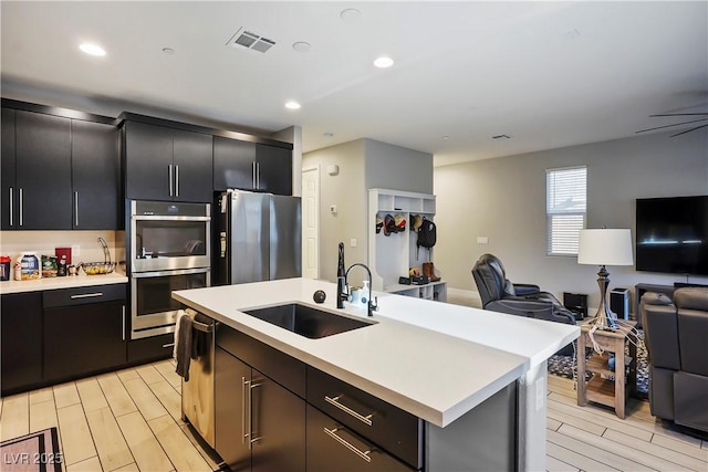 kitchen featuring ceiling fan, a kitchen island with sink, sink, and stainless steel appliances