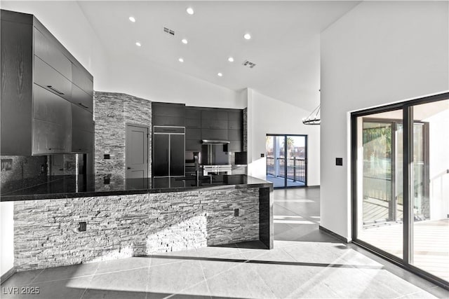 kitchen featuring sink, high vaulted ceiling, light tile patterned floors, dark stone counters, and paneled built in fridge