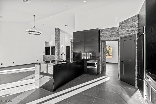 kitchen with a notable chandelier, oven, sink, a high ceiling, and dark tile patterned floors