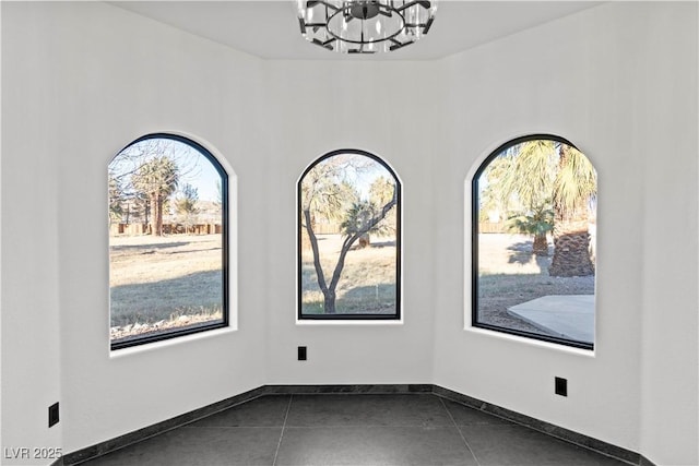 unfurnished room with an inviting chandelier, plenty of natural light, and dark tile patterned flooring