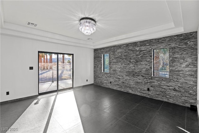 tiled empty room featuring a tray ceiling and a chandelier