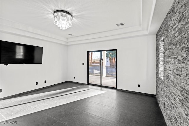 unfurnished living room featuring dark tile patterned flooring, a raised ceiling, and a notable chandelier